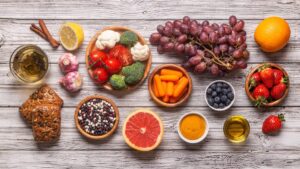 Alimentos antiinflamatorios sobre una mesa de madera: uvas, frutos rojos, cítricos, brócoli, tomates, legumbres, cúrcuma y aceite de oliva