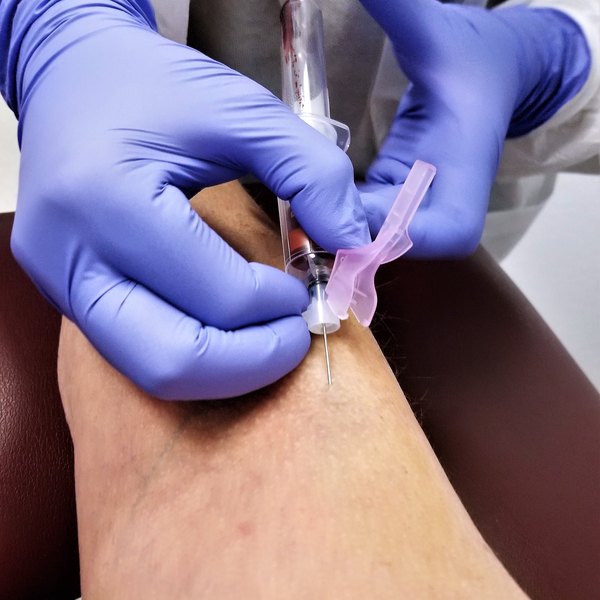 Manos con guantes extrayendo una muestra de sangre del brazo para una analítica