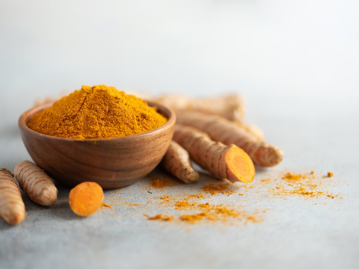 Cúrcuma en polvo en un cuenco de madera junto a raíces de cúrcuma fresca