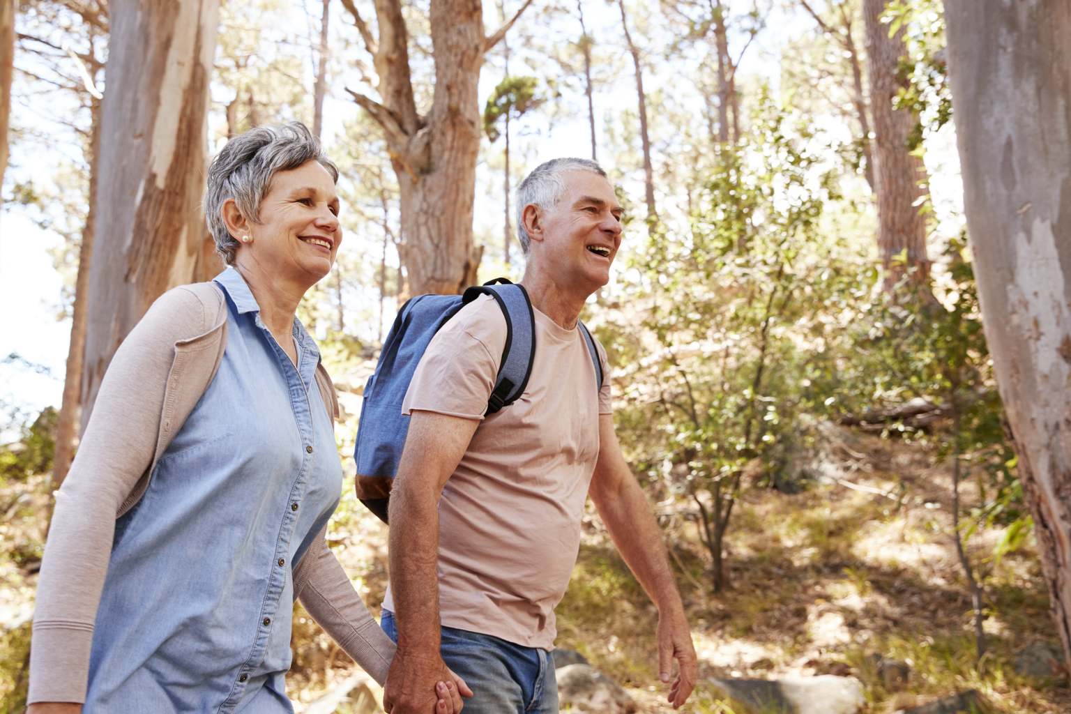 Pareja madura sonriente caminando de la mano por un sendero del bosque