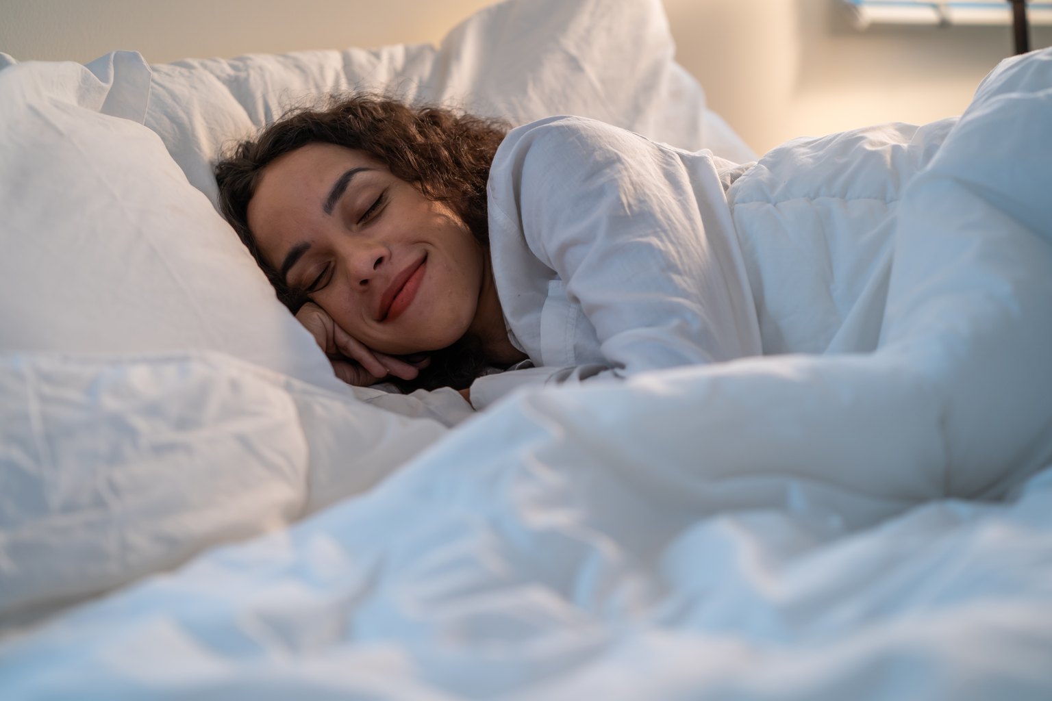 Mujer durmiendo plácidamente en su cama con sábanas blancas