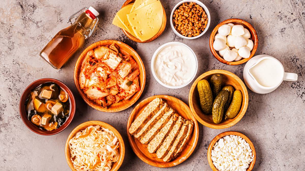 Alimentos fermentados vistos desde arriba: kimchi, chucrut, yogur, kéfir, tempeh, sopa de miso, queso, pepinillos y kombucha