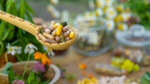 Cuchara de madera con cápsulas de suplementos entre hierbas y flores medicinales