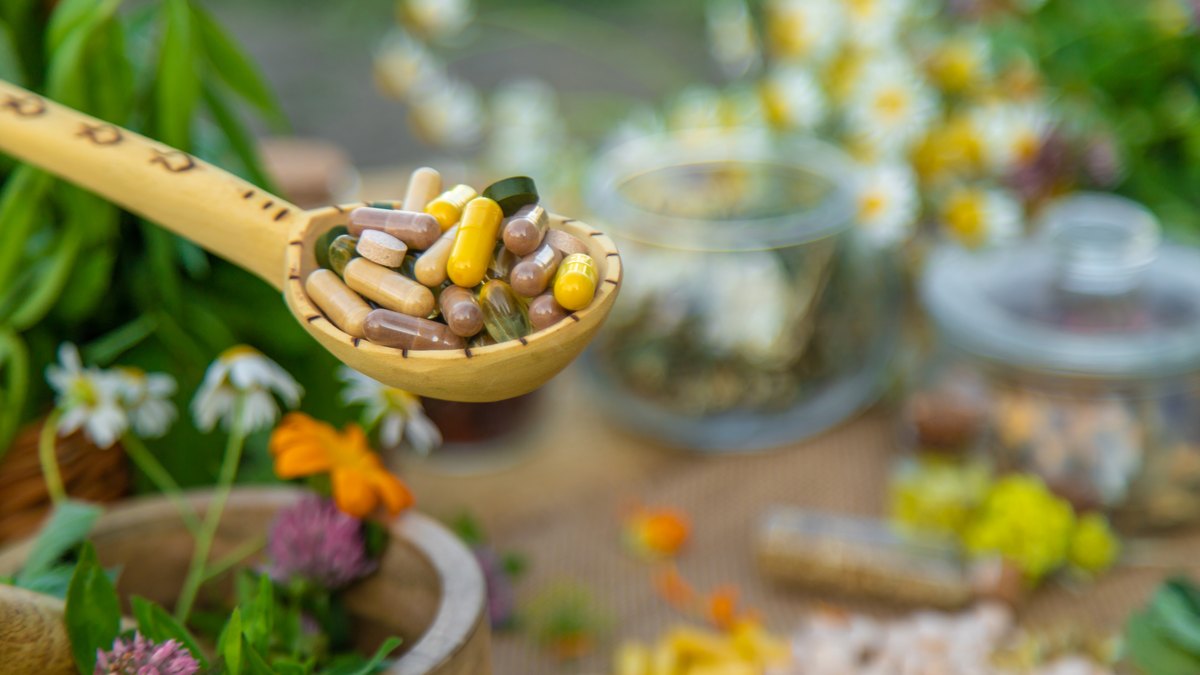 Cuchara de madera con cápsulas de suplementos entre hierbas y flores medicinales