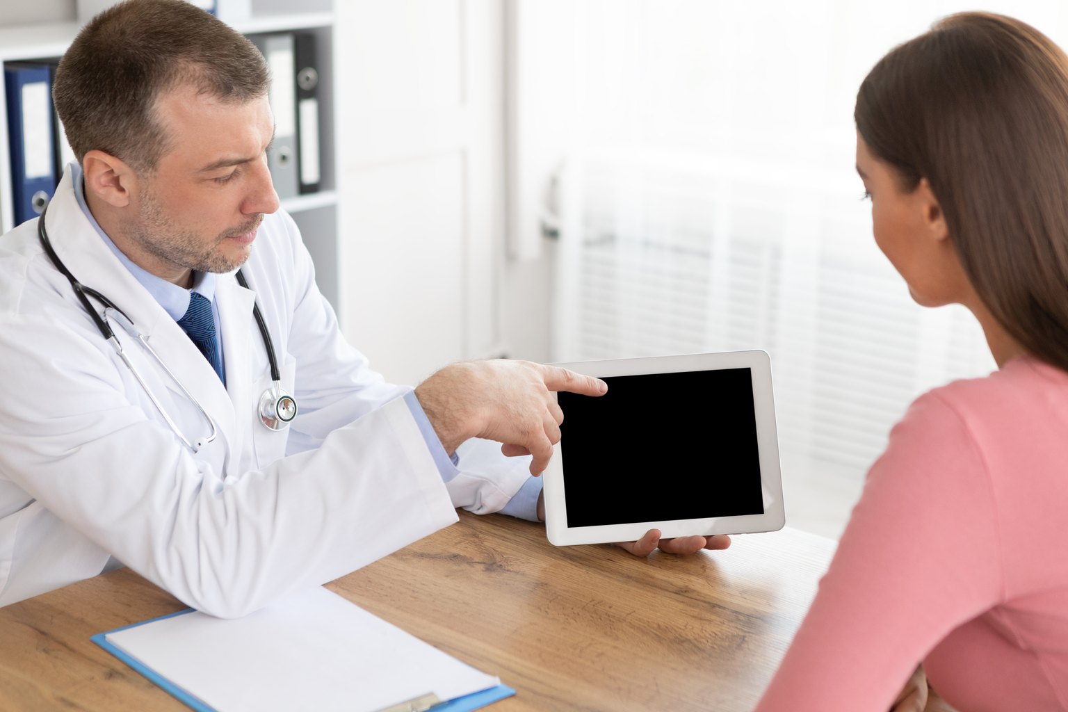 Médico explicando a una paciente su programa en una tableta durante la consulta